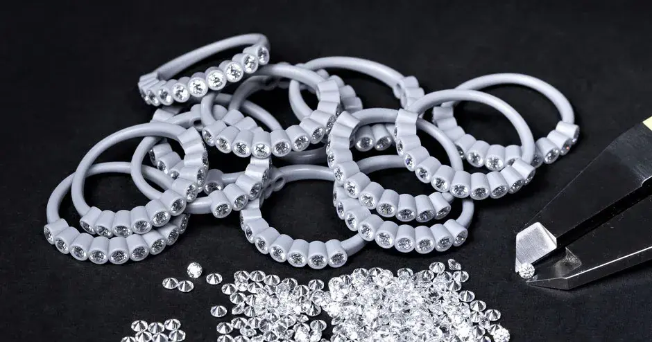 ダイヤモンドがセットされた多数のワックスモールドリング、カリパスの先端にはさまれたダイヤモンド、散らばったダイヤモンド