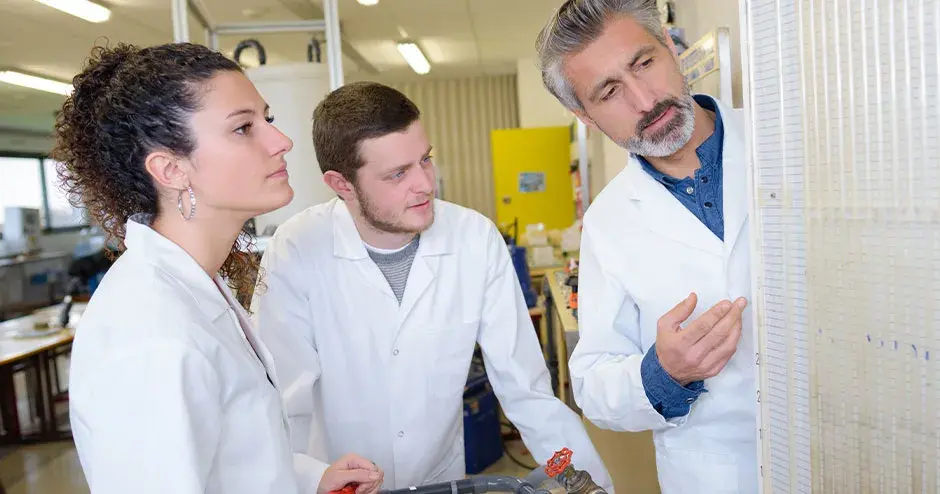 施設内で立って仕事について議論している 3 人