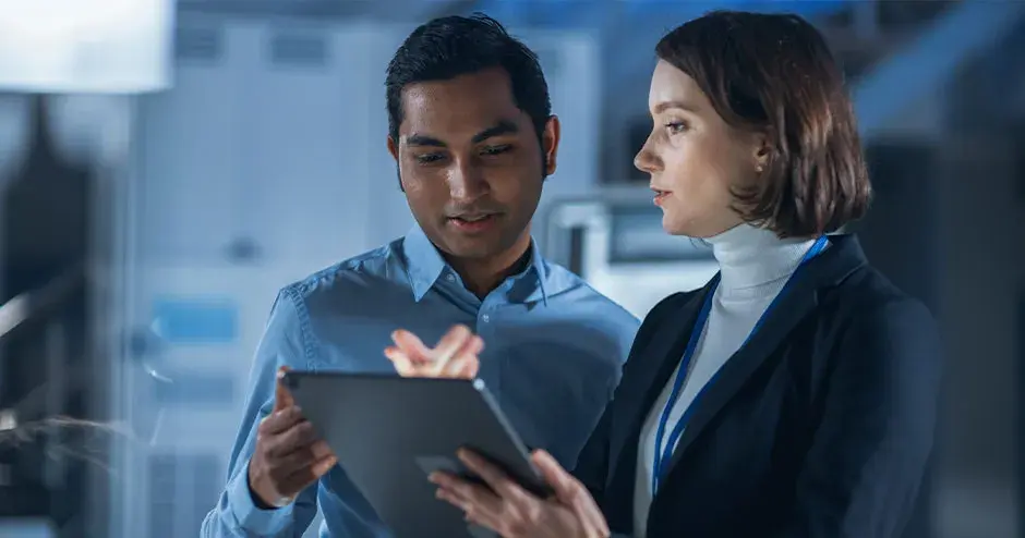 工場内でタブレットを使って共同作業している 2 人の人物